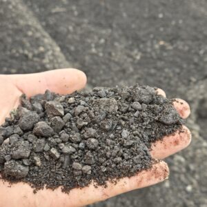20260416_105344 - wnyDIRT.com Handful of dark crushed rock or gravel held over a rough asphalt surface.