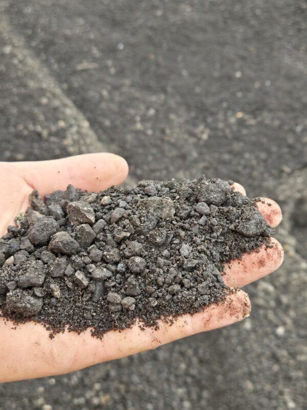 20260416_105344 - wnyDIRT.com Handful of dark crushed rock or gravel held over a rough asphalt surface.