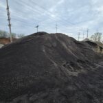20260416_105405 - wnyDIRT.com Large mound of black coal piled outdoors with power poles and lines in the background on a cloudy day.